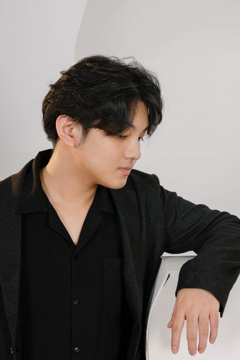 Portrait of a young adult man in a black shirt and blazer, indoors with a thoughtful expression.