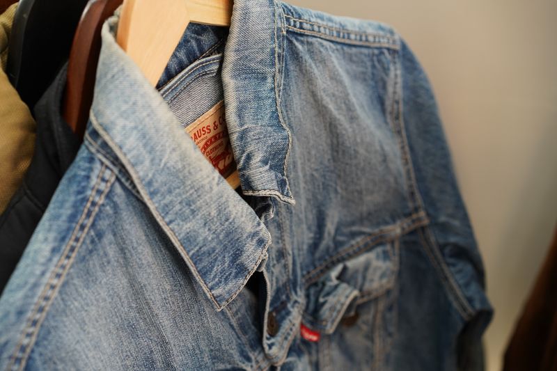 Close-up of a blue denim jacket hanging on a wooden hanger indoors.