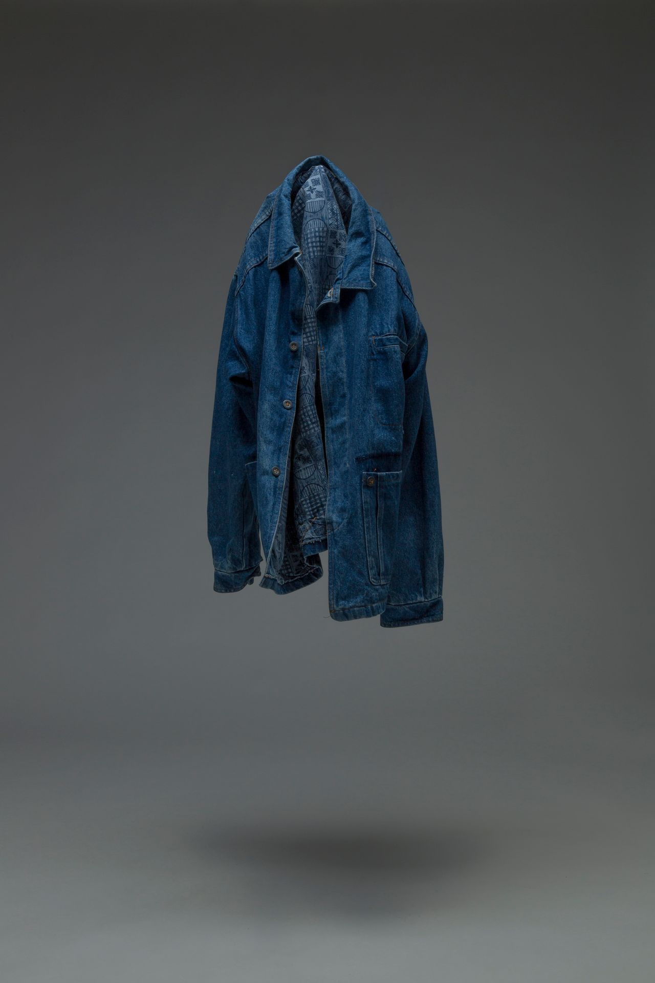 Minimalist image of a blue denim jacket suspended in midair against a gray backdrop.