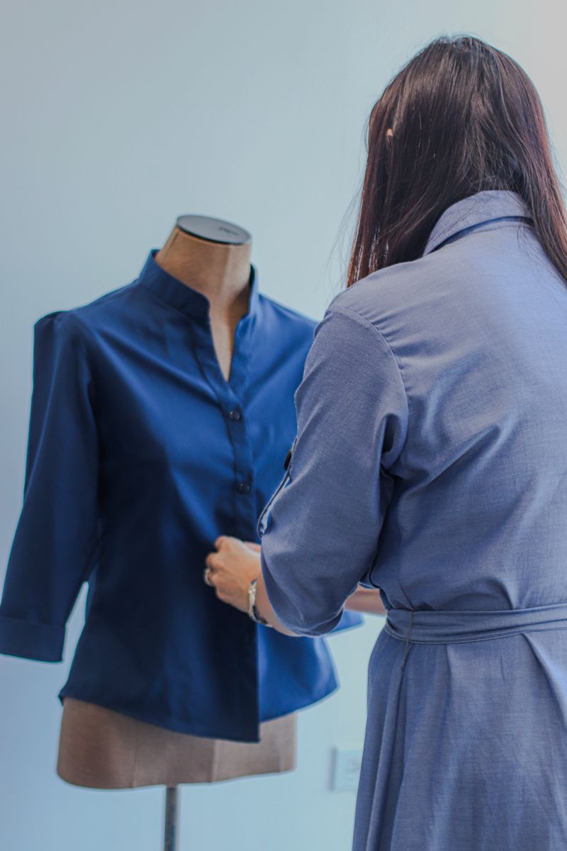 A fashion designer adjusts a blue blouse on a mannequin in a studio setting.