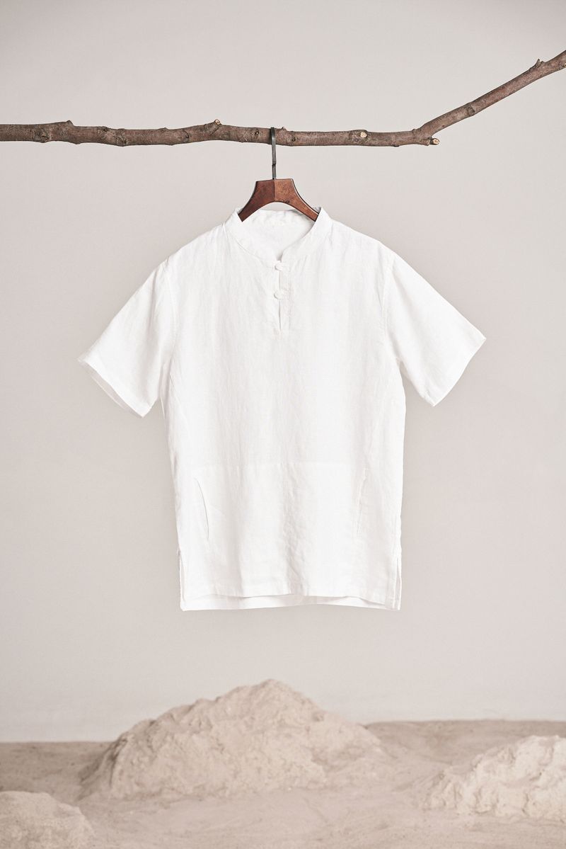 Stylish white shirt hanging on a natural wooden branch against a neutral background.