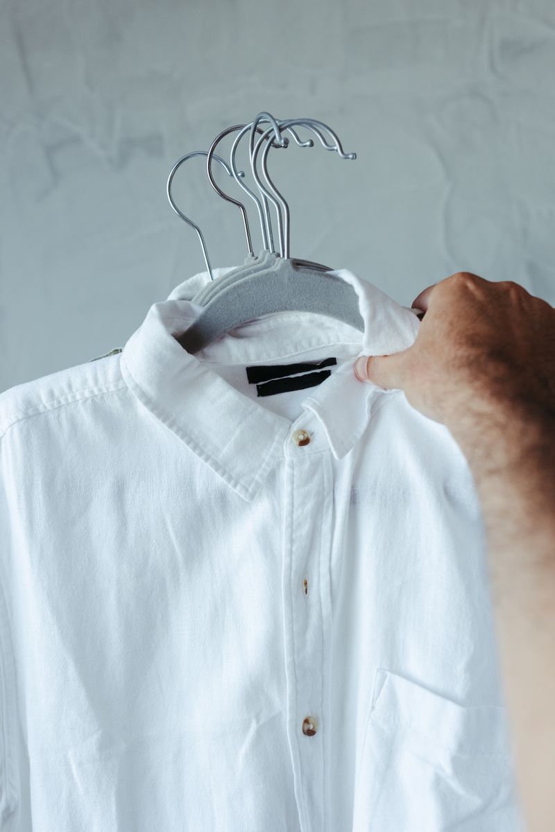 Close-up of a white shirt on a hanger in a minimalist setting.