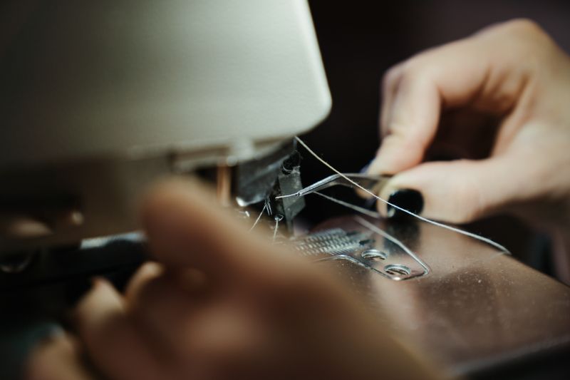 Close-up of hands threading a sewing machine in a workshop.