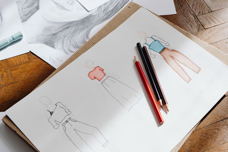 Artistic fashion design sketches on paper accompanied by colored pencils.