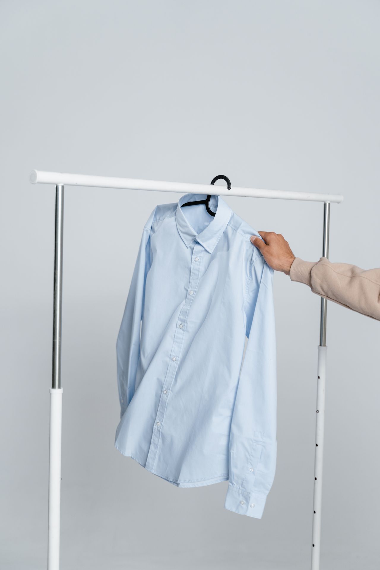 A person selects an elegant blue shirt on a hanger in a studio setting, showcasing office attire.